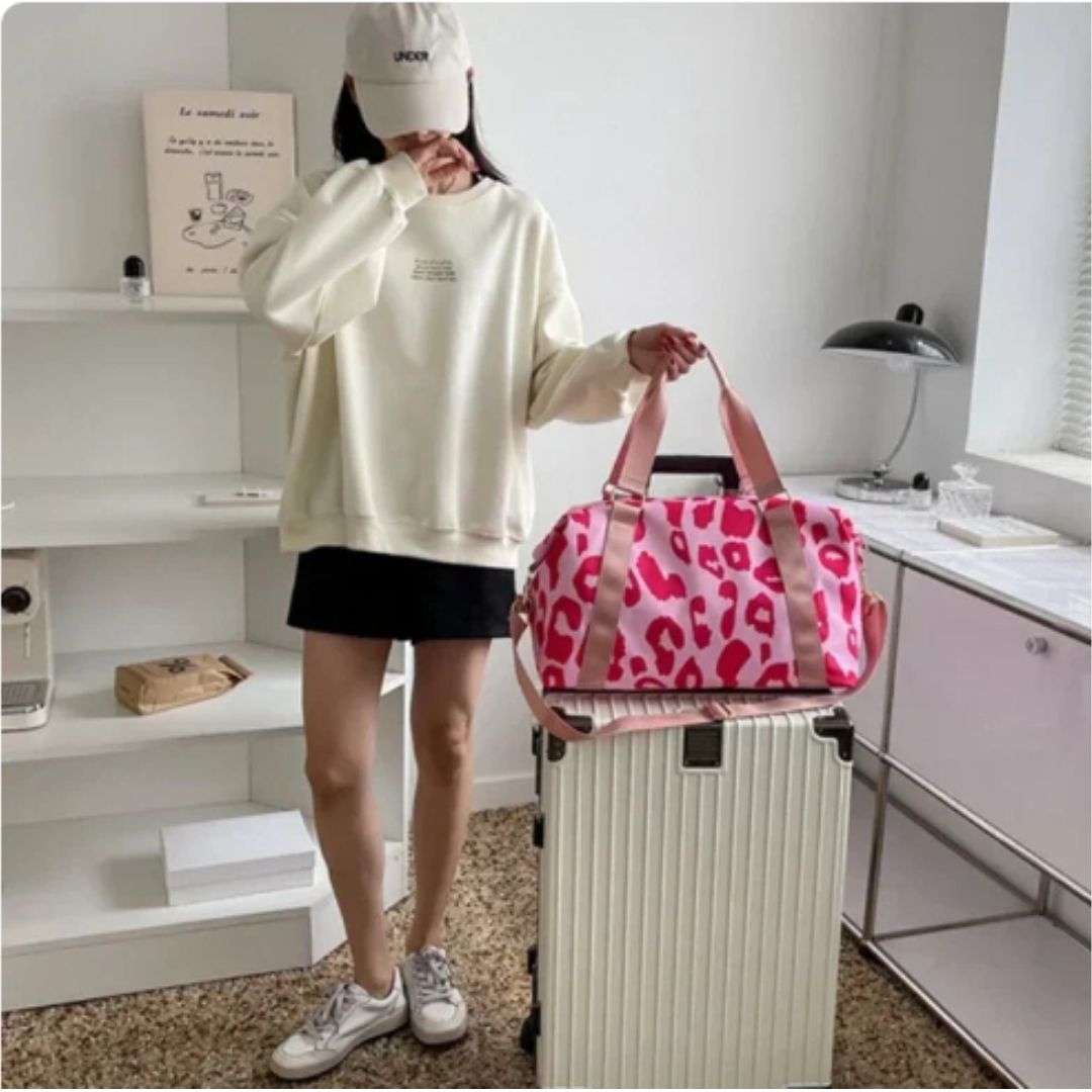 Young woman illustrating a red and pink leopard print travel duffel bag attached to a travel case